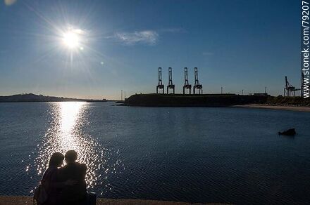 Silhouette of a couple sitting on the Sarandí breakwater in contrast with the reflection of the sun on the river. - Department of Montevideo - URUGUAY. Photo #79207
